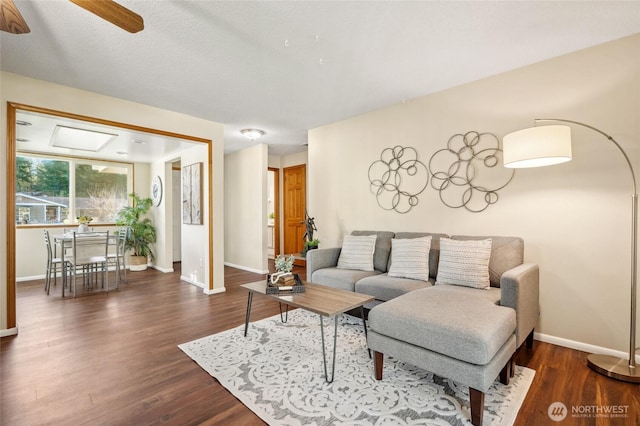 living area featuring ceiling fan, baseboards, and dark wood finished floors