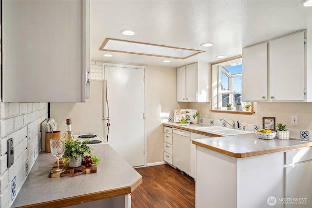 kitchen featuring dark wood-type flooring, a sink, a peninsula, light countertops, and dishwasher