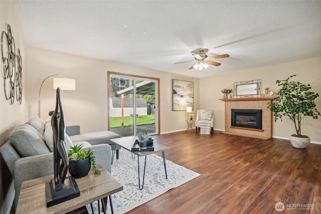 living room with a fireplace, a textured ceiling, baseboards, and wood finished floors