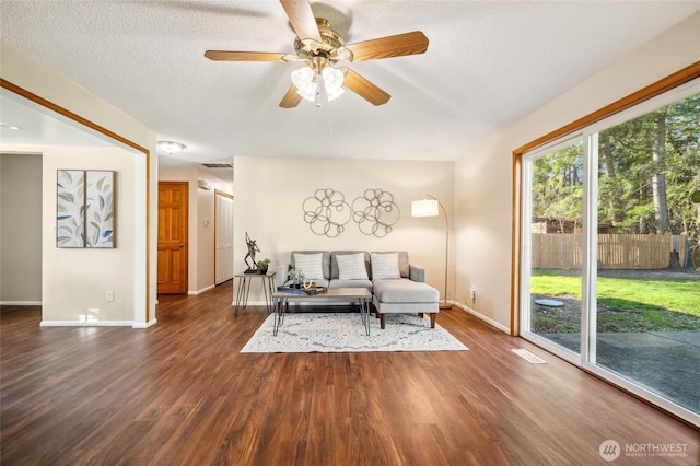 living area with a ceiling fan, visible vents, baseboards, dark wood finished floors, and a textured ceiling