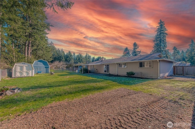 back of house at dusk featuring a yard, fence, an outdoor structure, and a shed