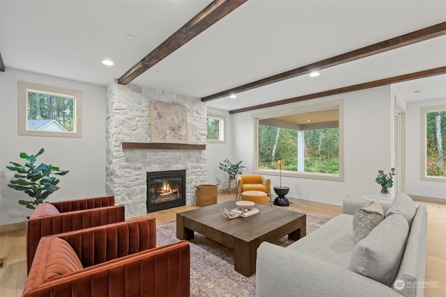 living room with beam ceiling, a stone fireplace, light hardwood / wood-style flooring, and a healthy amount of sunlight