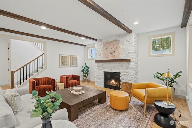 living room featuring wood-type flooring, a stone fireplace, and beam ceiling