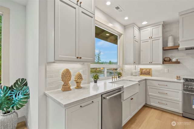 kitchen with appliances with stainless steel finishes, sink, backsplash, white cabinets, and light hardwood / wood-style floors