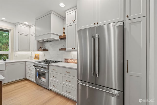 kitchen featuring high end appliances, white cabinetry, custom exhaust hood, and light hardwood / wood-style floors