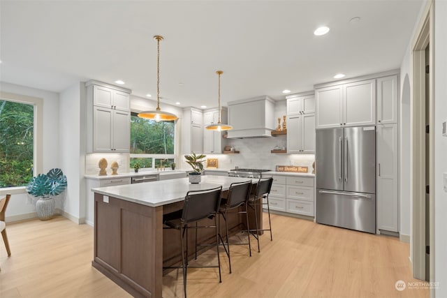 kitchen featuring a breakfast bar area, a center island, hanging light fixtures, light wood-type flooring, and appliances with stainless steel finishes