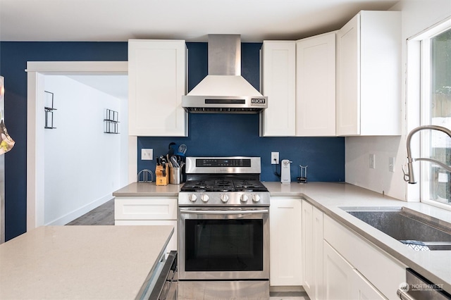 kitchen with white cabinetry, dishwasher, sink, stainless steel gas range oven, and wall chimney range hood