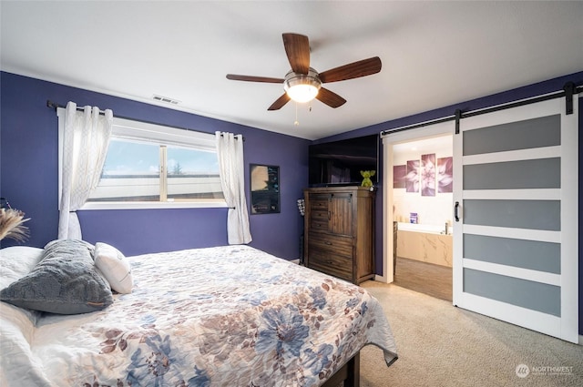 carpeted bedroom with a barn door, ceiling fan, and ensuite bathroom