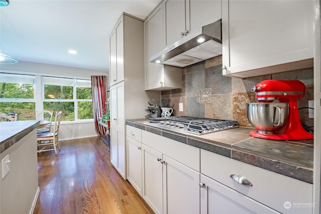 kitchen with stainless steel gas stovetop, white cabinets, light hardwood / wood-style floors, and decorative backsplash