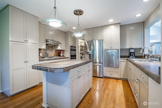 kitchen with a kitchen island, appliances with stainless steel finishes, decorative light fixtures, sink, and light hardwood / wood-style flooring