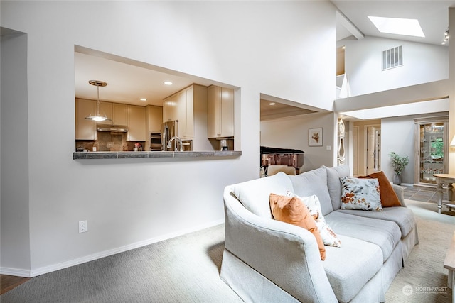 carpeted living room featuring a skylight and high vaulted ceiling