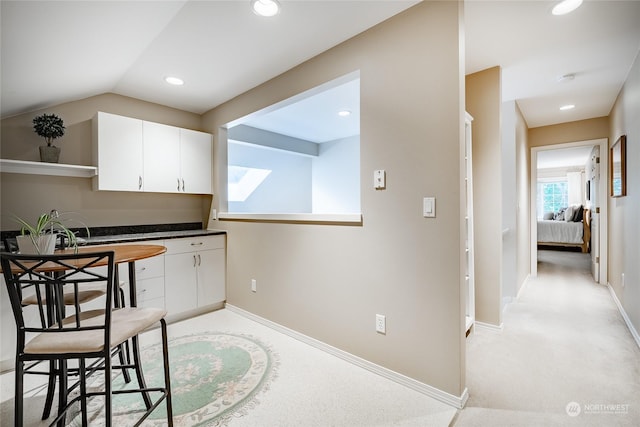 kitchen with white cabinetry, lofted ceiling, light carpet, and a kitchen breakfast bar