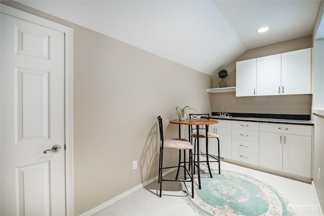 kitchen with white cabinetry, sink, and lofted ceiling