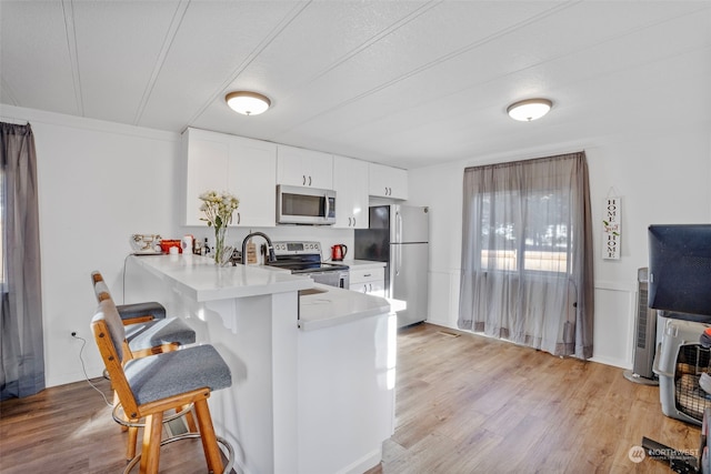 kitchen with appliances with stainless steel finishes, a kitchen breakfast bar, kitchen peninsula, light hardwood / wood-style floors, and white cabinets