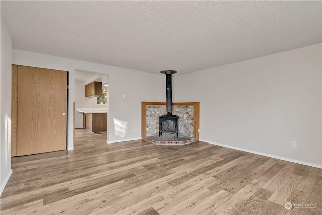 unfurnished living room featuring a wood stove, a textured ceiling, and light wood-type flooring