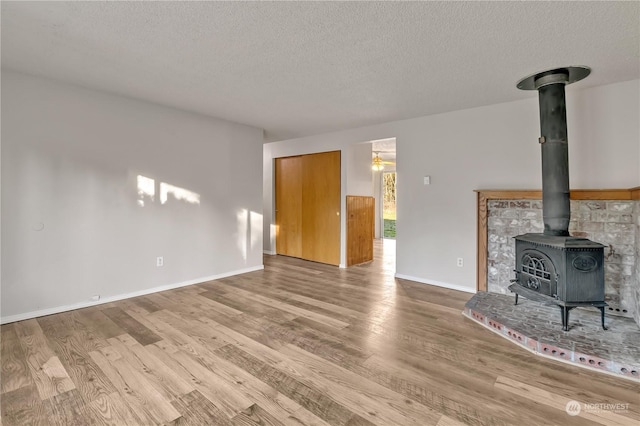 unfurnished living room featuring light wood-type flooring, a textured ceiling, and a wood stove