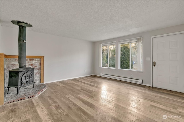 unfurnished living room with a baseboard radiator, a wood stove, hardwood / wood-style floors, and a textured ceiling