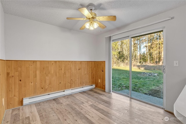 unfurnished room featuring wood walls, light hardwood / wood-style flooring, a textured ceiling, and a baseboard heating unit