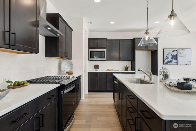 kitchen with sink, light hardwood / wood-style flooring, stainless steel microwave, range with gas stovetop, and wall chimney exhaust hood