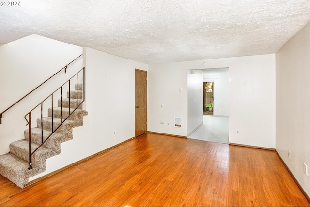 unfurnished room with visible vents, a textured ceiling, stairway, and wood finished floors