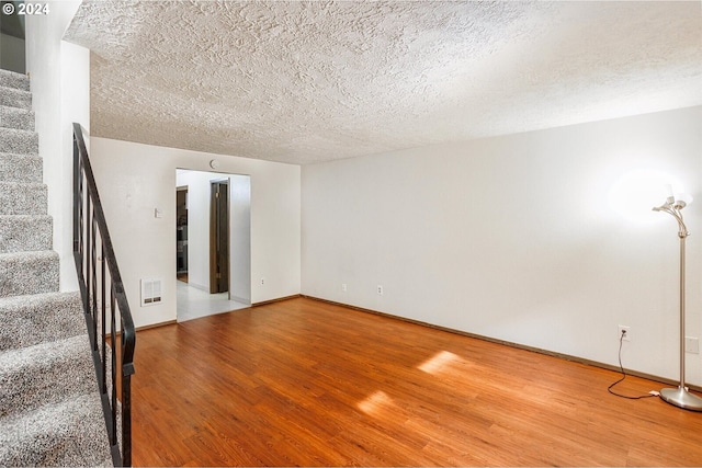 unfurnished living room with baseboards, visible vents, wood finished floors, stairs, and a textured ceiling