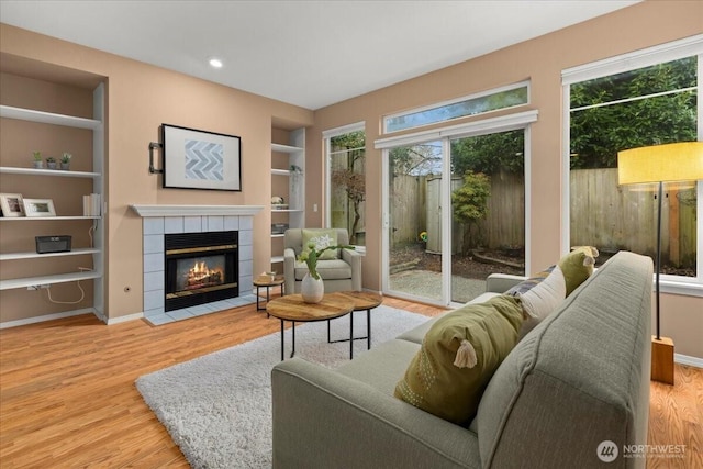 living area featuring built in shelves, recessed lighting, a fireplace, wood finished floors, and baseboards