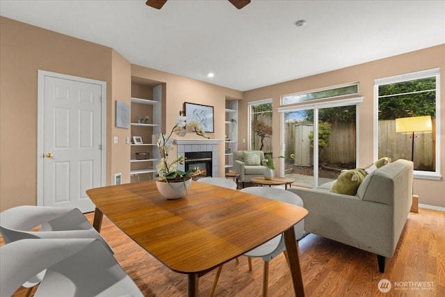 living room featuring light wood-style floors, built in features, plenty of natural light, and a tiled fireplace