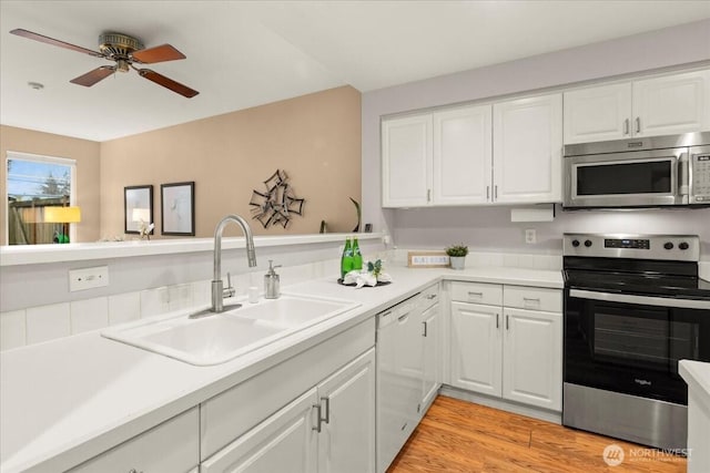 kitchen featuring white cabinets, stainless steel appliances, light countertops, light wood-type flooring, and a sink