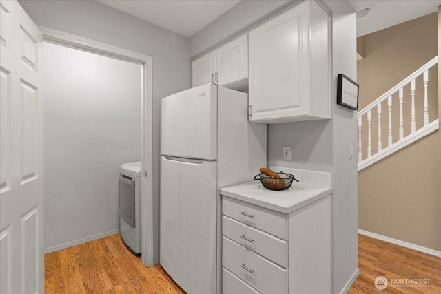 kitchen with light countertops, light wood finished floors, freestanding refrigerator, and white cabinetry