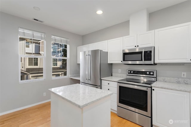 kitchen with stainless steel appliances, light stone countertops, light hardwood / wood-style floors, white cabinets, and a kitchen island