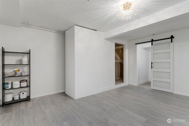 unfurnished room with an inviting chandelier, light hardwood / wood-style flooring, and a barn door