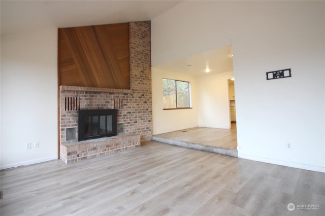 unfurnished living room with a brick fireplace, high vaulted ceiling, and light wood-type flooring