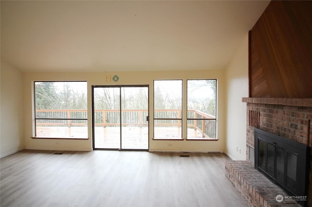 unfurnished living room with vaulted ceiling, a fireplace, and light hardwood / wood-style floors