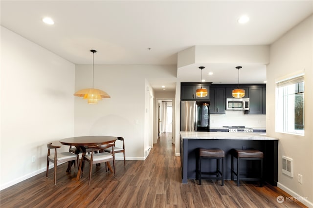 kitchen with pendant lighting, appliances with stainless steel finishes, backsplash, light stone countertops, and a kitchen bar