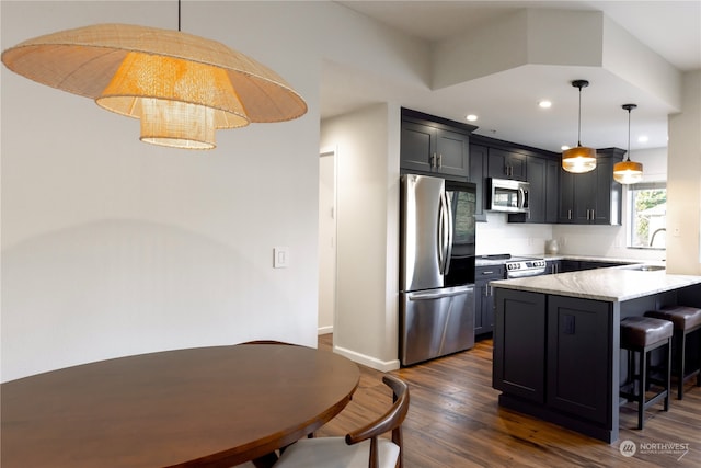 kitchen featuring pendant lighting, dark wood-type flooring, a breakfast bar area, appliances with stainless steel finishes, and kitchen peninsula