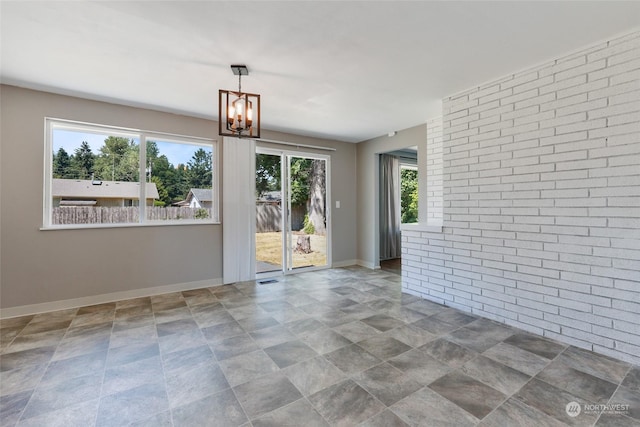 spare room with an inviting chandelier and brick wall