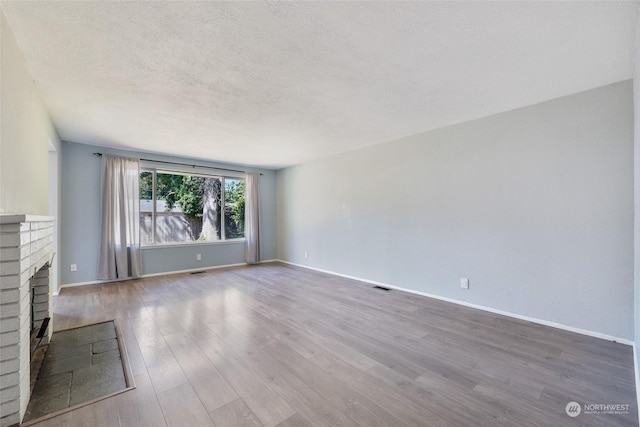 unfurnished living room with a brick fireplace, hardwood / wood-style floors, and a textured ceiling