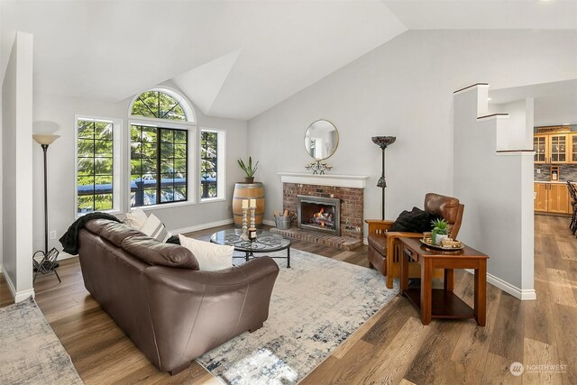 living area with lofted ceiling, a brick fireplace, baseboards, and wood finished floors