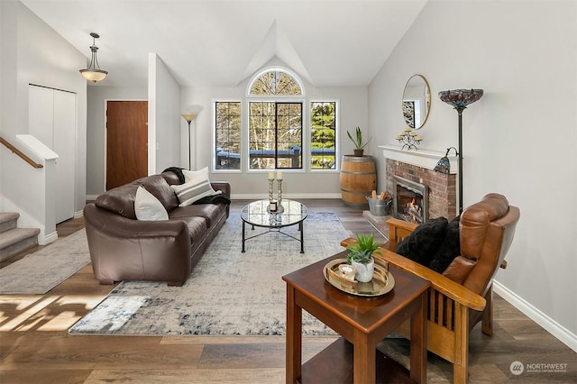 living area featuring a brick fireplace, stairway, vaulted ceiling, and wood finished floors