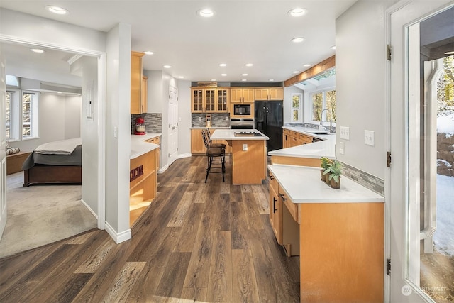 kitchen with a breakfast bar area, dark wood-type flooring, a sink, black appliances, and glass insert cabinets