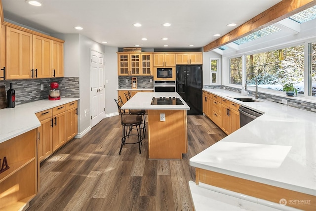 kitchen featuring dark wood-style floors, a kitchen island, black appliances, a kitchen bar, and a sink