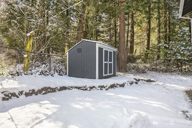 snow covered structure with an outbuilding, a storage unit, and fence