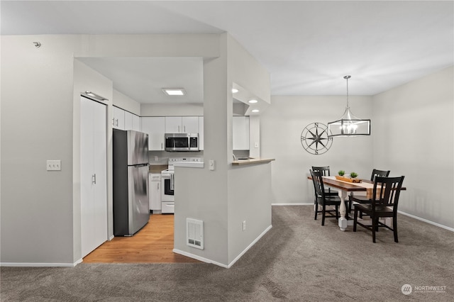 kitchen featuring stainless steel appliances, hanging light fixtures, light colored carpet, and white cabinets