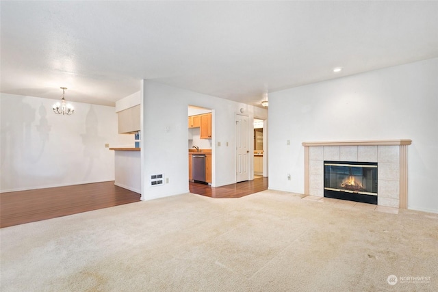 unfurnished living room featuring an inviting chandelier, a fireplace, and light colored carpet