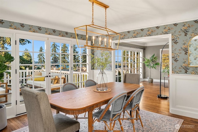 dining room featuring wood-type flooring, ornamental molding, an inviting chandelier, and french doors