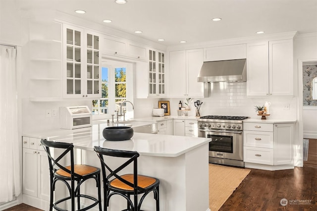 kitchen with high end range, white cabinetry, a breakfast bar, and wall chimney exhaust hood