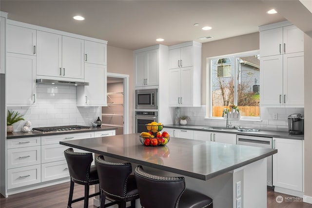 kitchen featuring a kitchen island, white cabinets, a kitchen bar, stainless steel appliances, and dark wood-type flooring