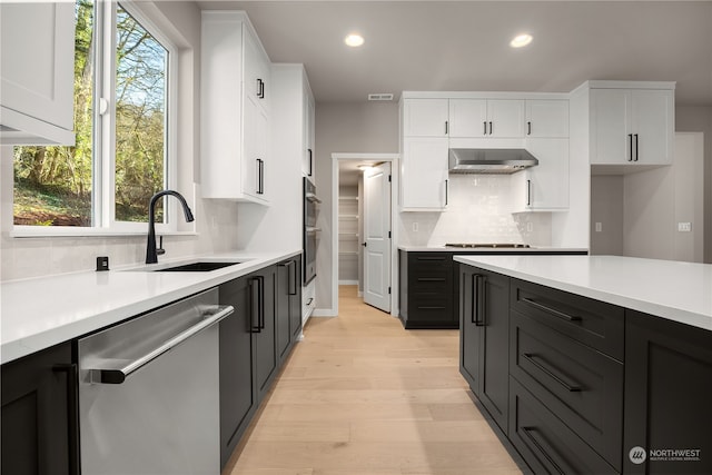 kitchen featuring a sink, stainless steel appliances, wall chimney exhaust hood, and white cabinetry