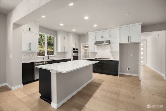 kitchen with a kitchen island, appliances with stainless steel finishes, white cabinetry, wall chimney exhaust hood, and a sink