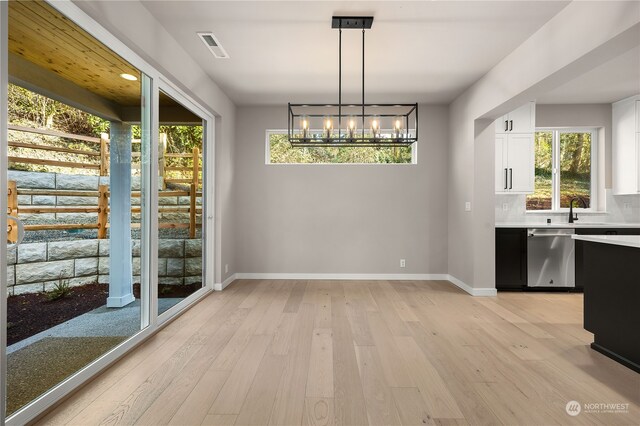 unfurnished dining area with visible vents, baseboards, a notable chandelier, and light wood finished floors